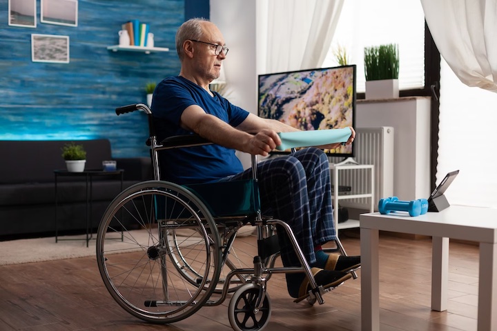 A multiple sclerosis patient in wheelchair exercising while sitting with a stretching band in his hands.