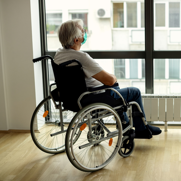 A senior multiple sclerosis patient in wheelchair looking through the window.