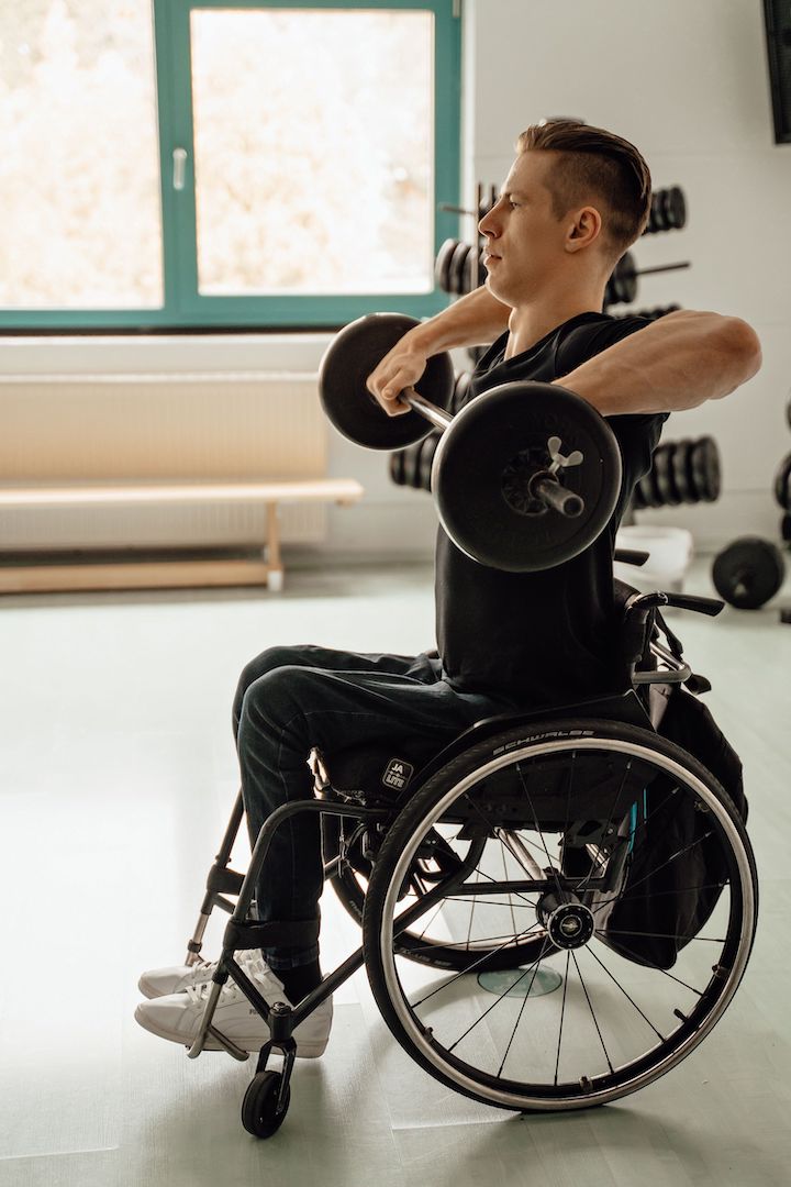 An athletic but disabled man in wheelchair lifting a bar with some weights.