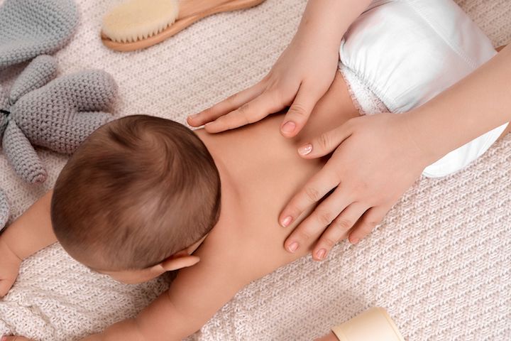A baby on its tummy being massaged on his back by a physical therapy.