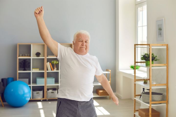 An smiling positive elderly man stretching as part of a home exercise for flexibility.