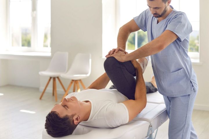 A physiotherapy specialist helping a male athlete do physical exercise during rehabilitation after a leg injury.
