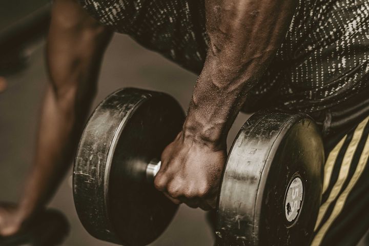 Close-up photo of a male person lifting a dumbbell with his left hand.