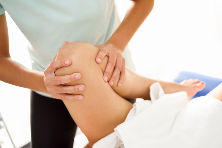 A massage being done to administer thigh pain on a patient with unrecognisable people.