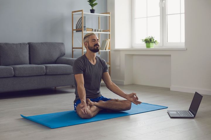 A male yoga practitioner smiling during a meditation session from an online class.