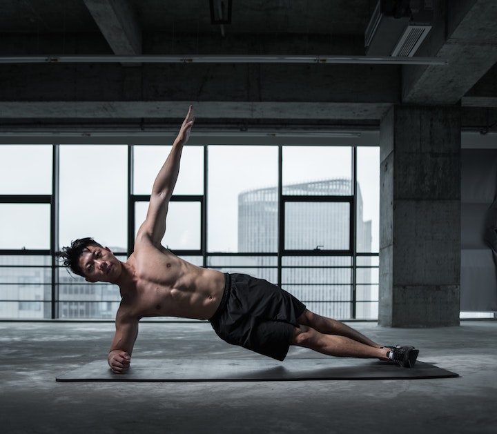 An athletic young Asian man performing a static balance exercise in a mat in an empty-like loft.