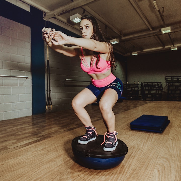 A sporty woman squatting and balancing herself on a BOSU ball.