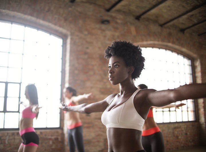 A fit ethnic woman training balance with other sportswomen in a modern fitness studio.