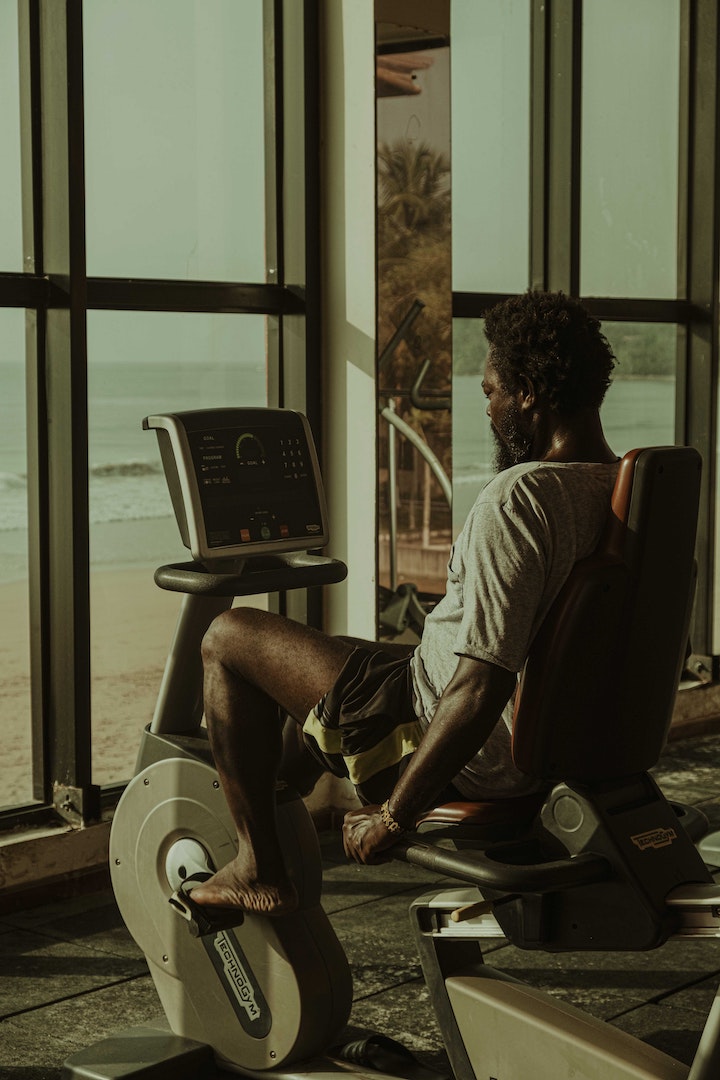 [Photoshoot from the back] An ethnic man using a cardio machine while exercising and tracking his vitals on the screen.
