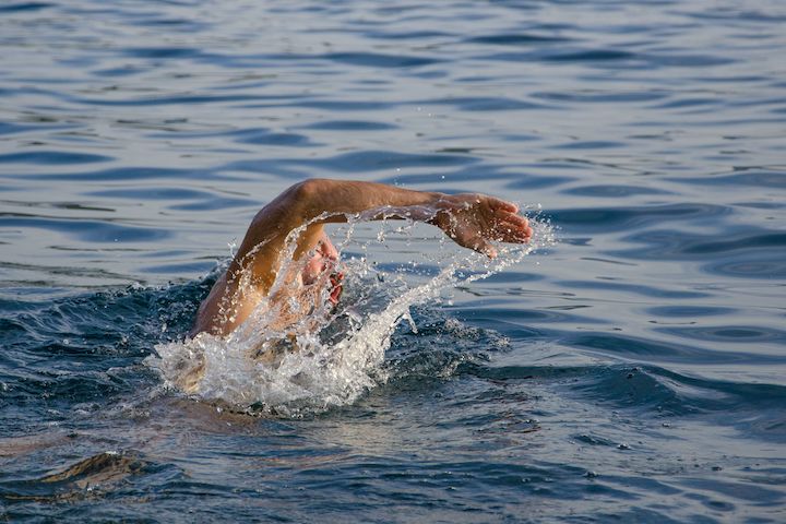 An unrecognisable person swimming on a body of water doing freestyle moves.