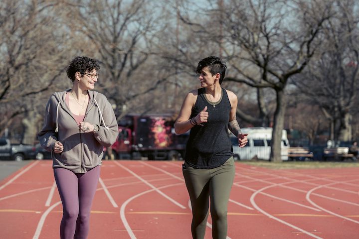 Two young fit women jogging on a racetrack.