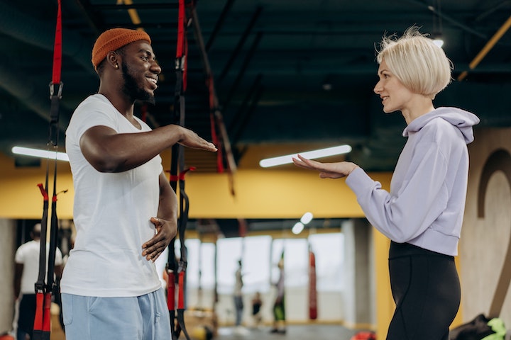 A Black man and a Caucasian woman discussing something in gym environment.