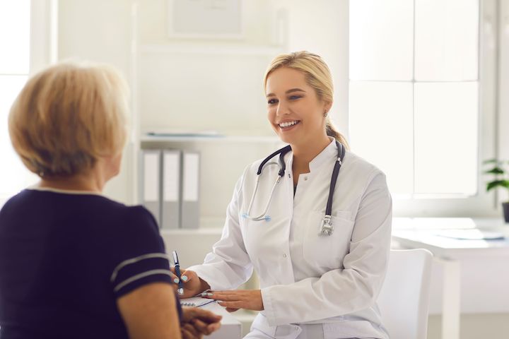 A female doctor smiling as she consults with an unrecoginsable patient.