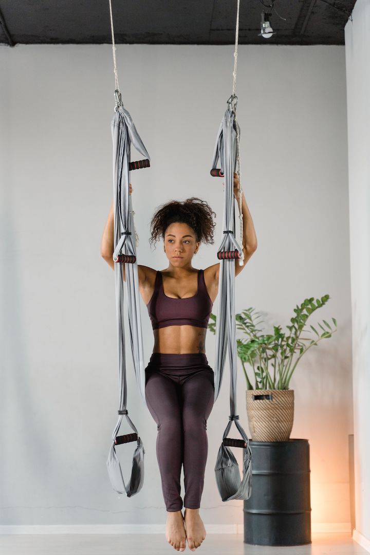 A multiracial woman in the midst of performing Pilates with the assitance of an equipment.