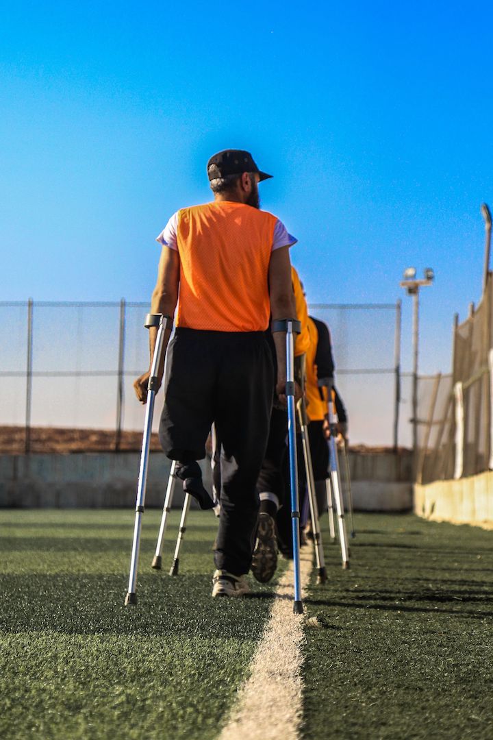 [Back view] A line of disabled patients walking with the help with crutches in a football field-like pitch.