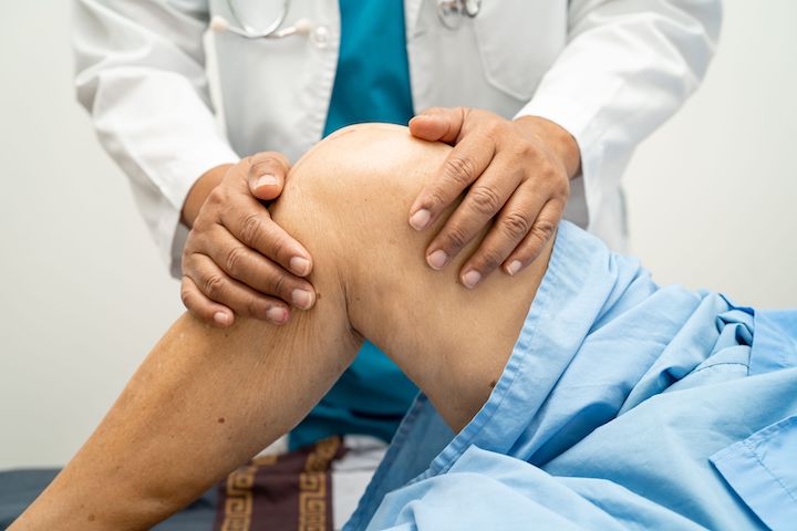 A physiotherapist examining and massaging the knee and thigh area of a patient.