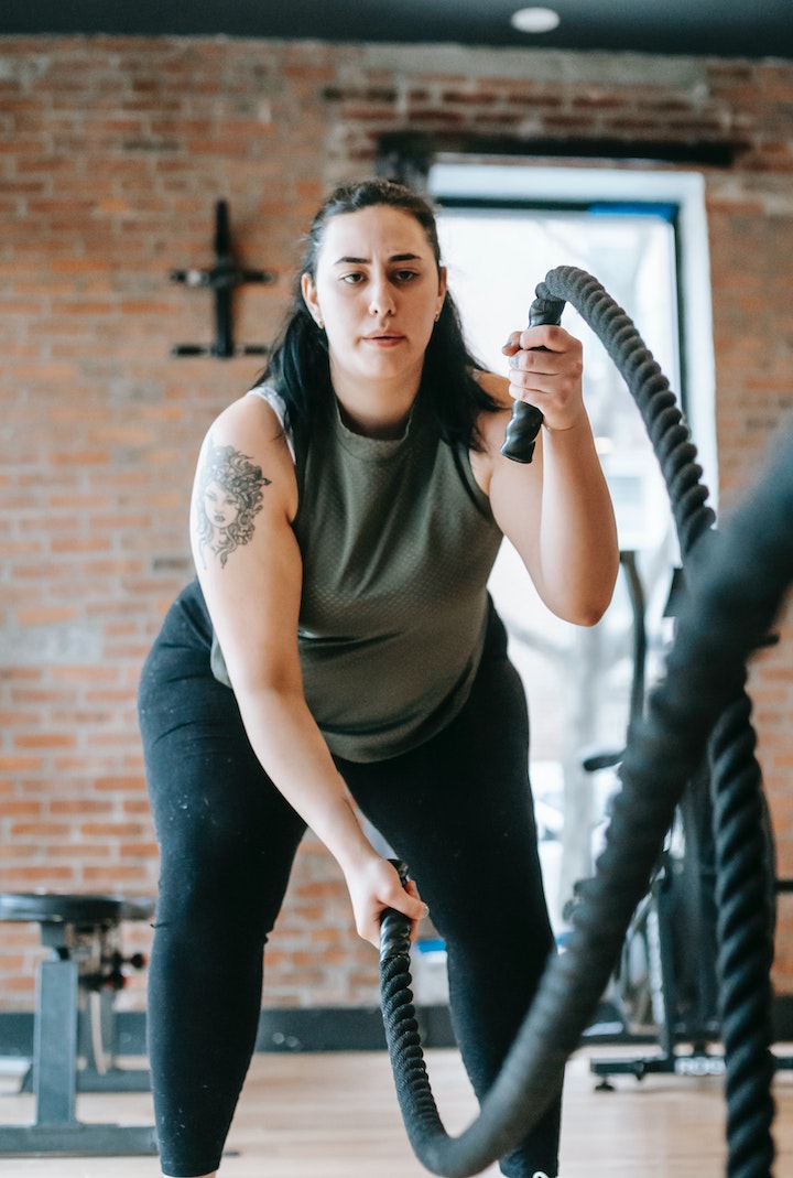 Chubby strong woman exercising with battle ropes in gym.