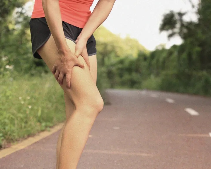 An unrecognisable runner holding her thigh during a run from an unexpected injury.