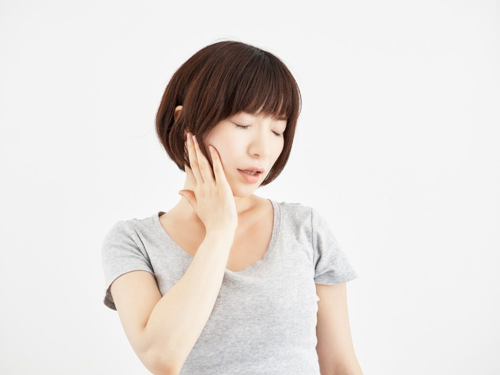 A woman holding down a sore jaw on a white background (Headache, neck & jaw pain).