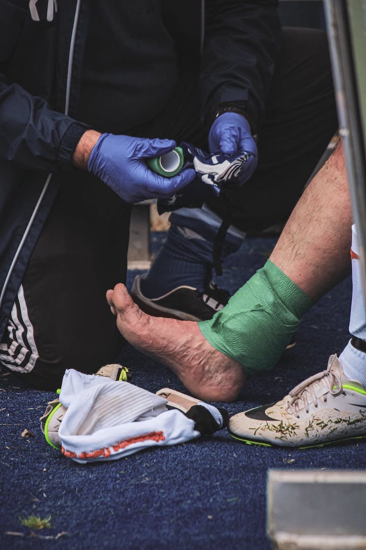 An unrecognisable injured footballer being bandaged in the ankle area after being injured during a game.