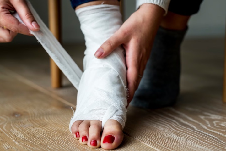 A female leg being bandaged by herself focusing on a heel injury area.