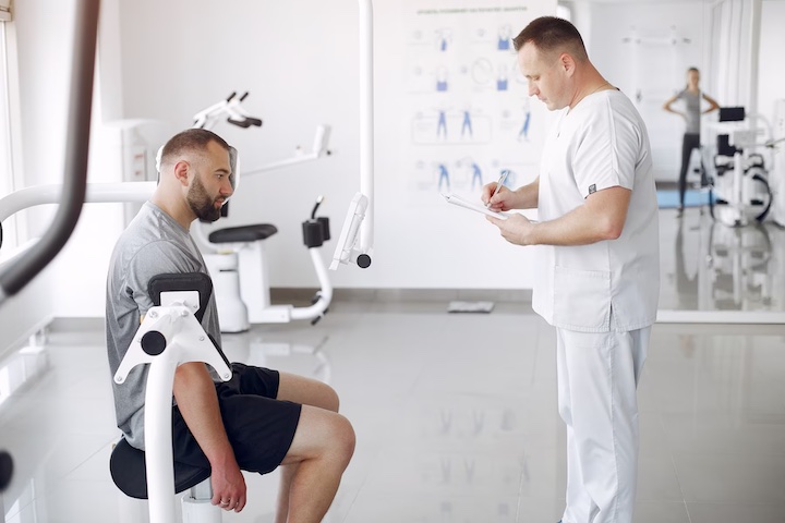 A physiotherapist taking notes as a patient sits without an expression in his face.