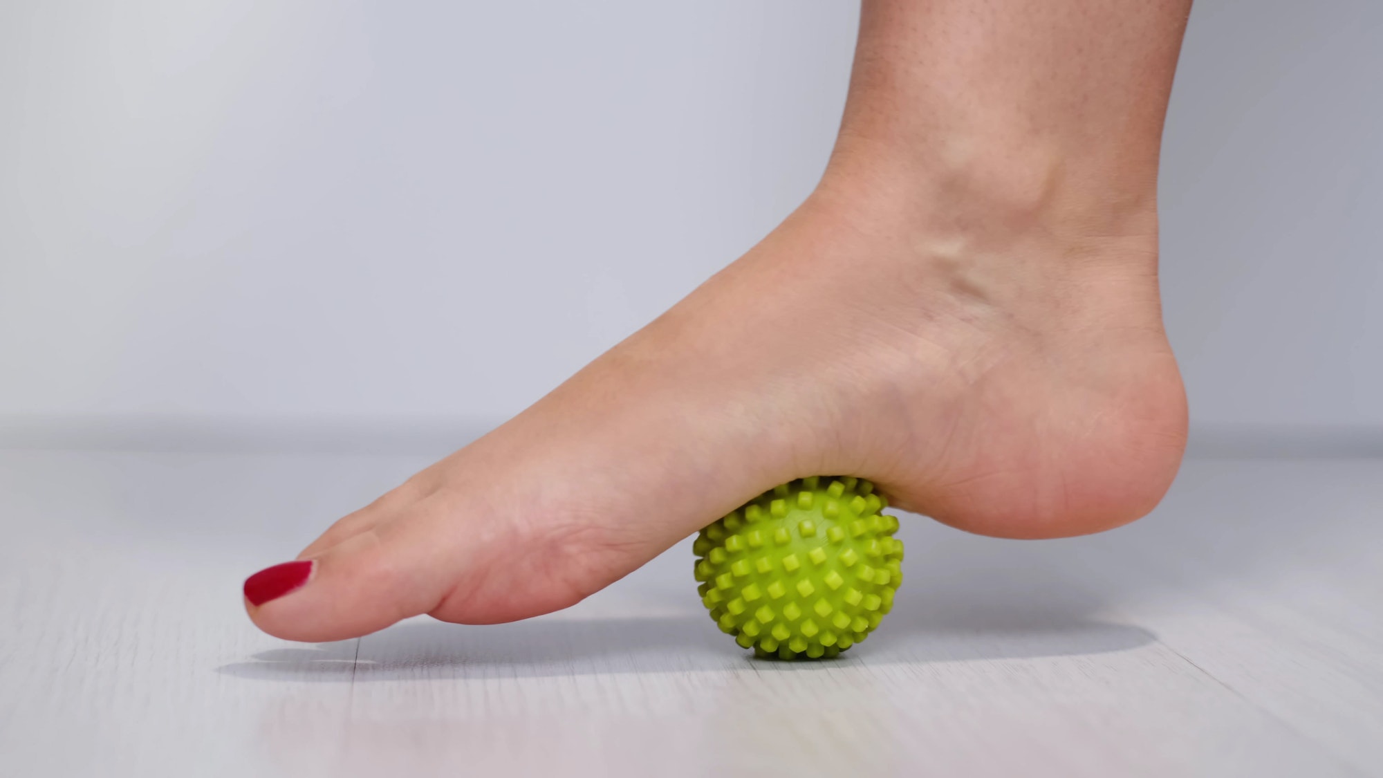 foot step on massage ball to relieve Plantar fasciitis or heel pain. woman with red