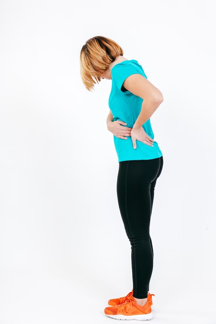 A woman in green T-shirt holding her lateral hip area while standing up.