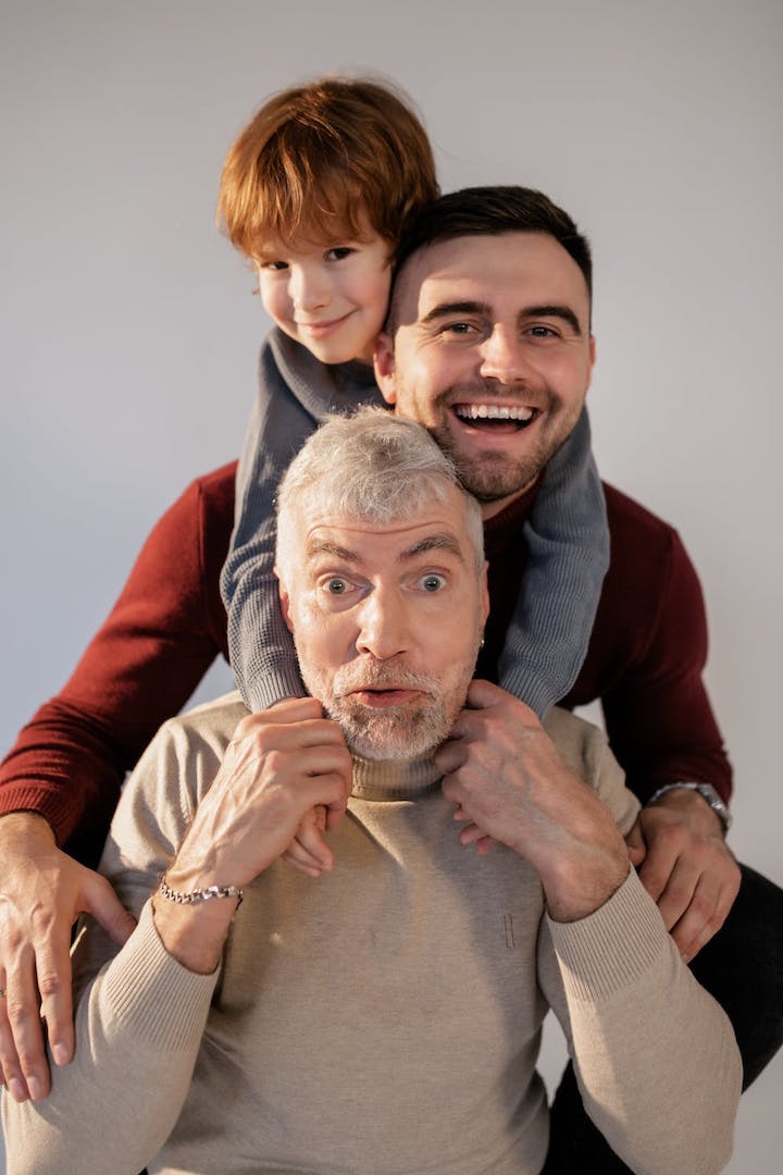 Three generations of male family members lining up with hugs from behind in a seated position, from grandpa to grandson.
