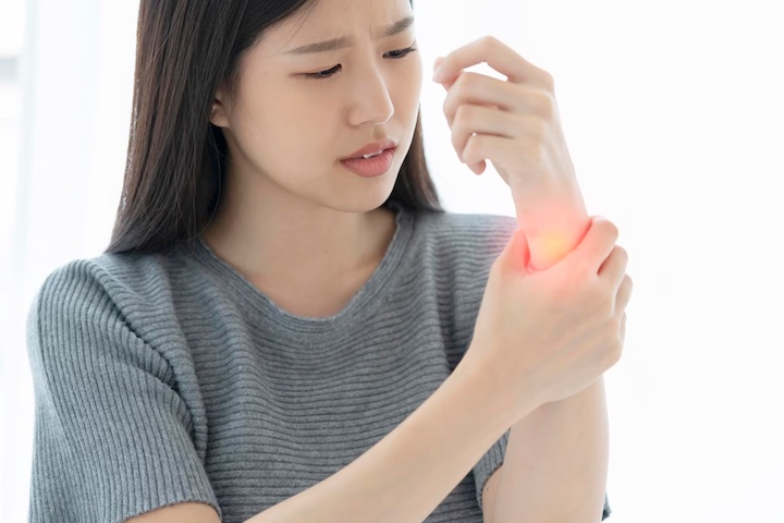 An Asian woman looking at and holding her wrist in pain photoshopped in red mark.