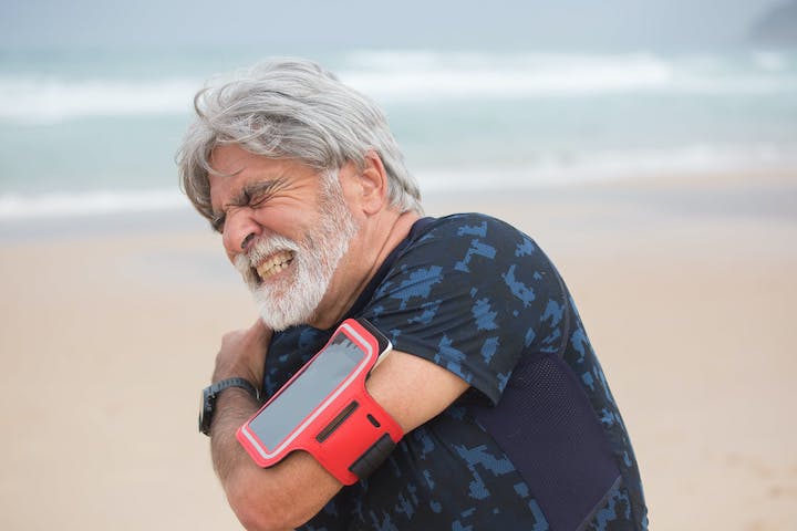 A middle-aged to elderly man shrugging because of his shoulder with a beachside background.