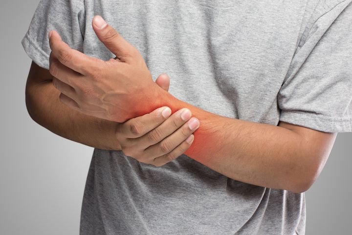 A male person holding his wrist with a photoshopped red mark where pain is supposed to have happened.