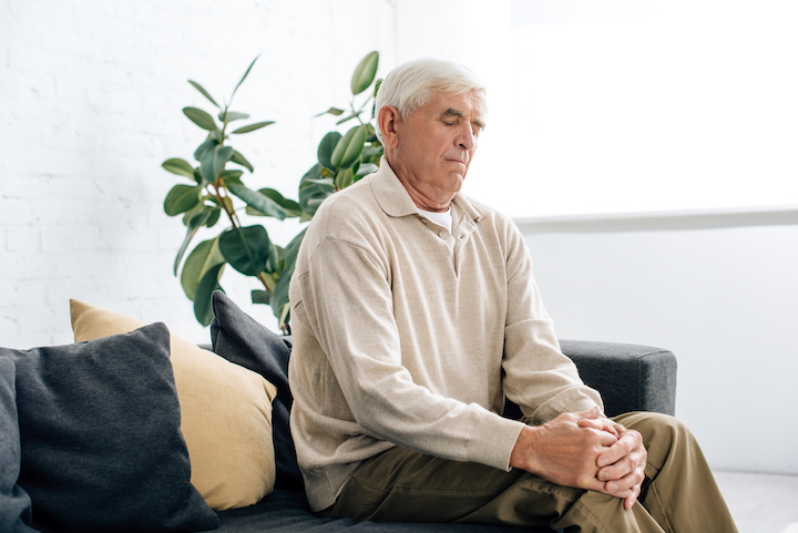senior man sitting on sofa and having knee Arthritis in apartment.