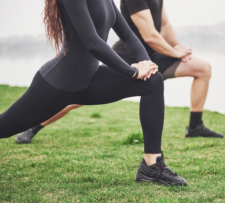 Close-up of a couple (without faces shown in the photo) doing lunges for his knees outdoors.