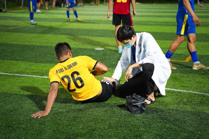 A medical professional tending to the injured knee of a football/soccer player while on the field.