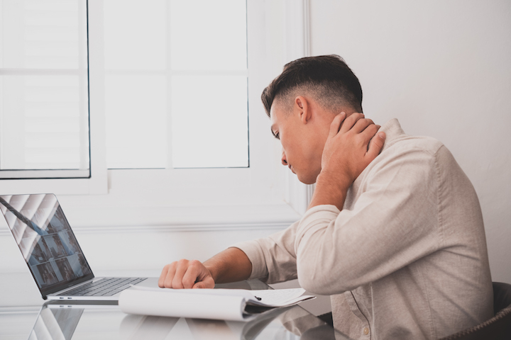 Close up rear view stressed young man touching lower neck feeling discomfort, suffering from sudden pain due to sedentary lifestyle or long computer overwork in incorrect posture at home office.