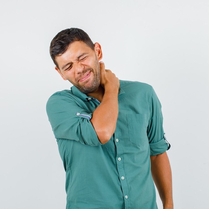 A young man in a green buttoned shirt squirming in pain in his neck.