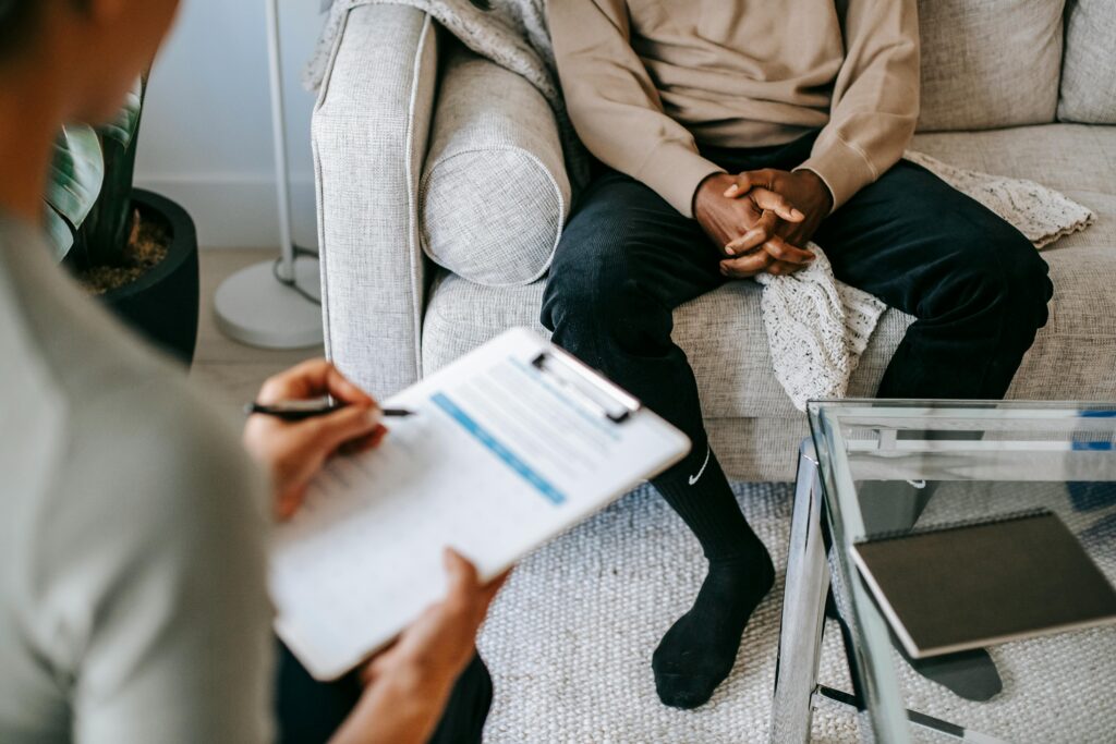  A man and woman sit on a couch, the man holding a clipboard as they address health concerns.
