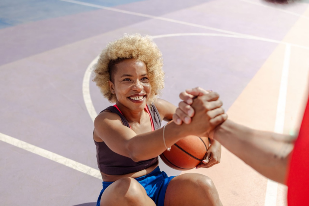  A woman holds a basketball while shaking hands, emphasizing sportsmanship and injury prevention in athletics.