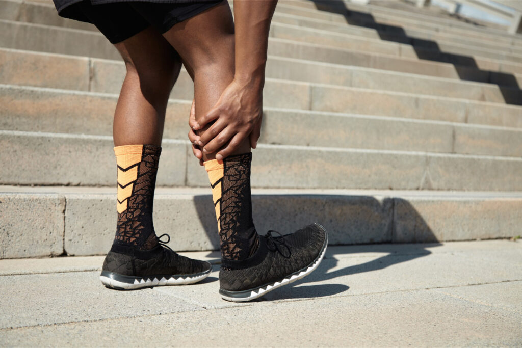 A man wearing a black and orange sock on his leg, highlighting calf strain issues and common causes.