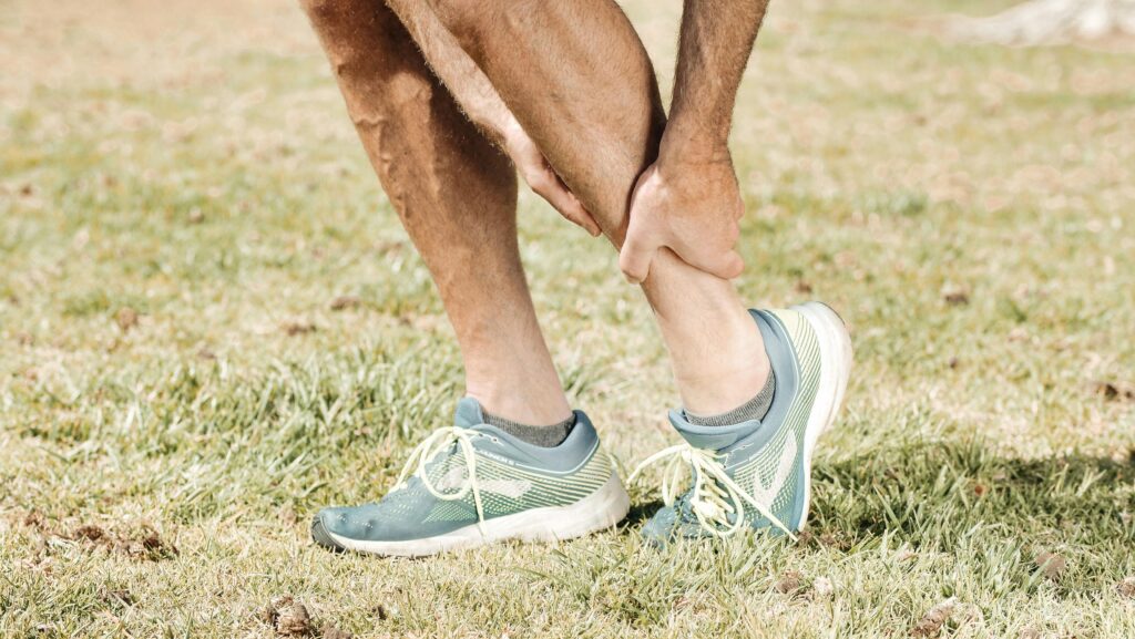  A man performs a leg stretch on the grass, focusing on alleviating calf strain discomfort and improving flexibility.
