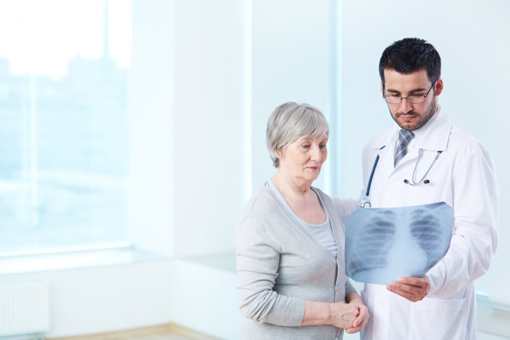  A doctor examines an X-ray with an older woman, discussing diagnosis methods for posture-related chest pain.