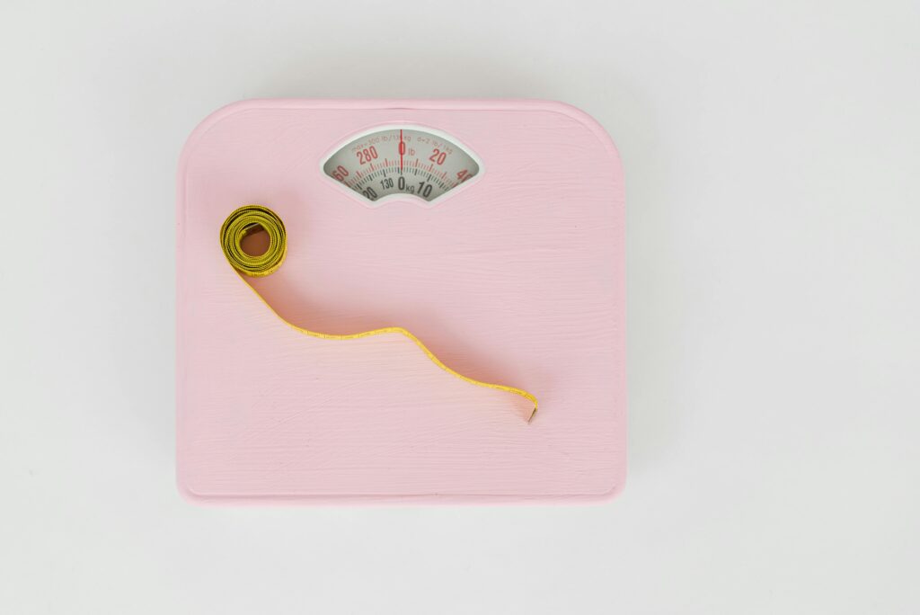 A pink scale with a yellow tape on it, symbolizing an evidence-based approach to weight loss.