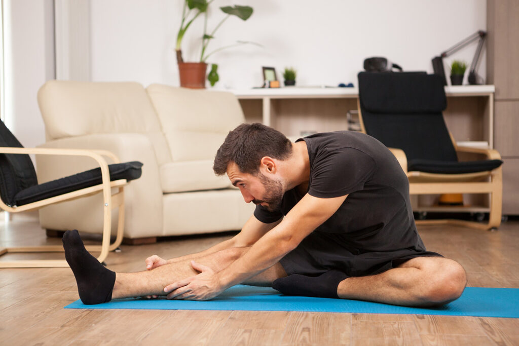 A man stretches his leg on a yoga mat, focusing on exercises to strengthen his knee and reduce clicking sounds.