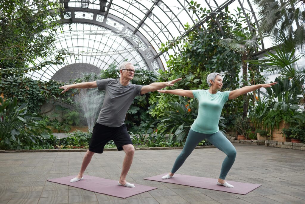 Two individuals practicing yoga in a serene greenhouse, surrounded by lush plants and natural light.