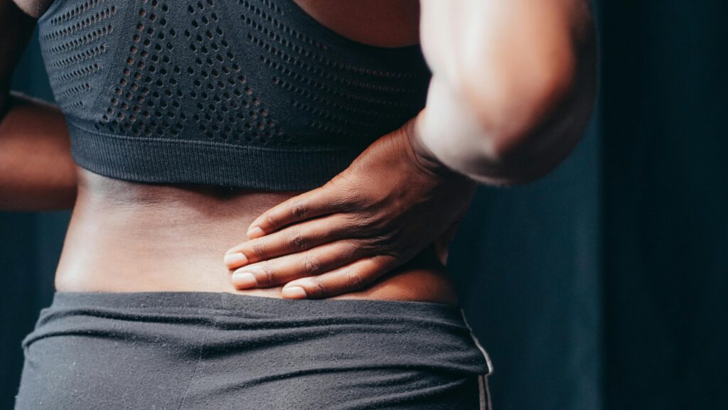 A woman experiencing back pain clutches her stomach, highlighting the need for physiotherapy in managing pain and discomfort.