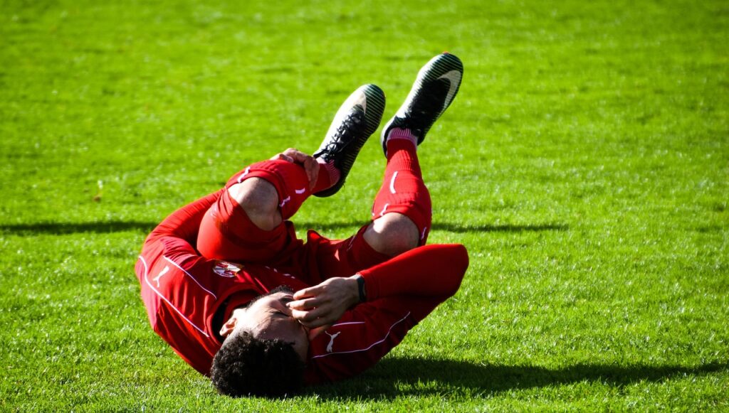 A soccer player lies on the ground, showing signs of injury during a match, emphasizing the initial steps after injury.
