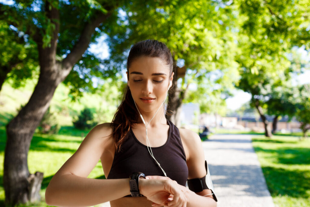 A woman checks her watch while enjoying music, reminding herself to stay active and maintain a healthy lifestyle.