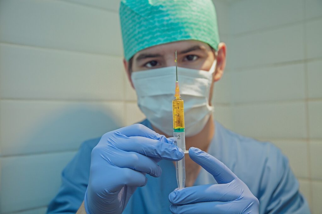  A man in a surgical mask and gloves prepares to administer a syringe for medications and injections.