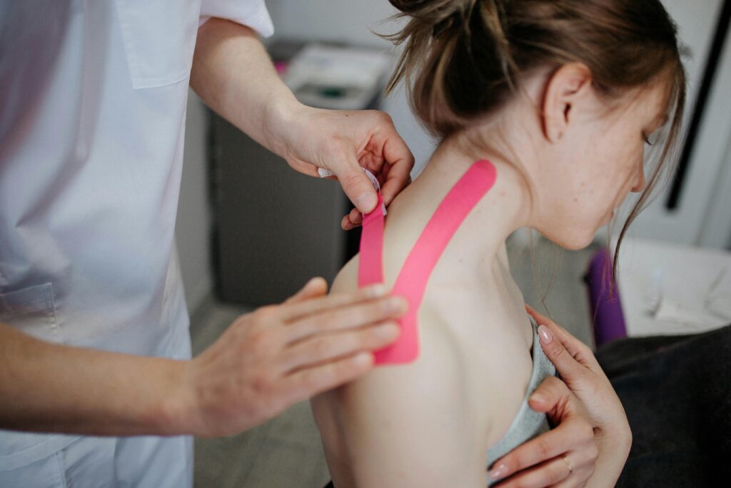 A physiotherapist applies pink tape to a woman's neck for therapeutic support and injury recovery.